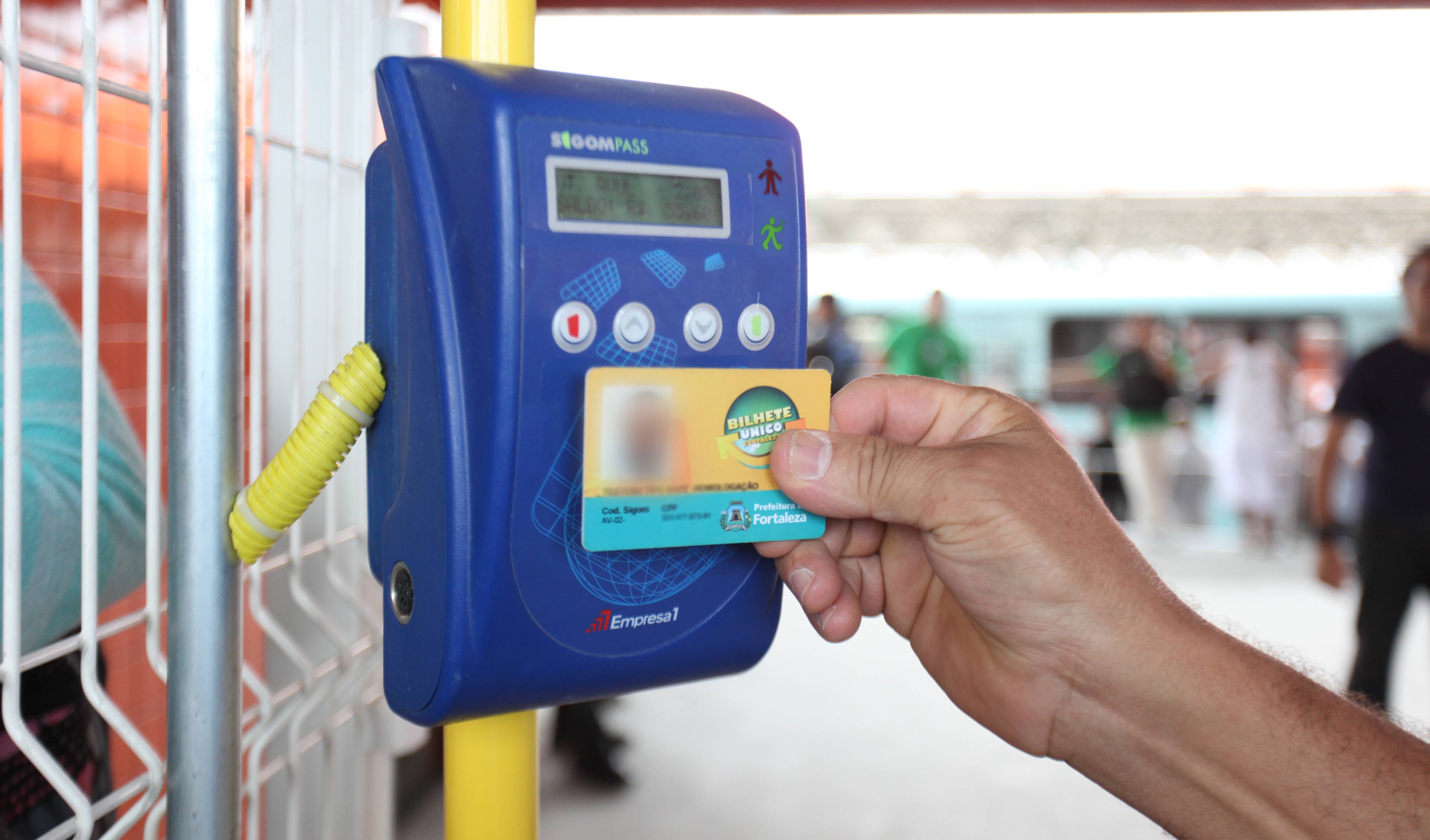 a foto mostra a mão de uma pessoa, que não aparece, passando o bilhete único por um leitor de cartões na entrada de um terminal